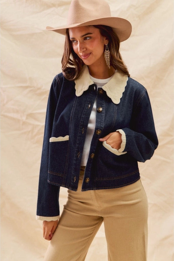 Woman wearing a denim jacket with white collar, beige hat, and pants against a beige background