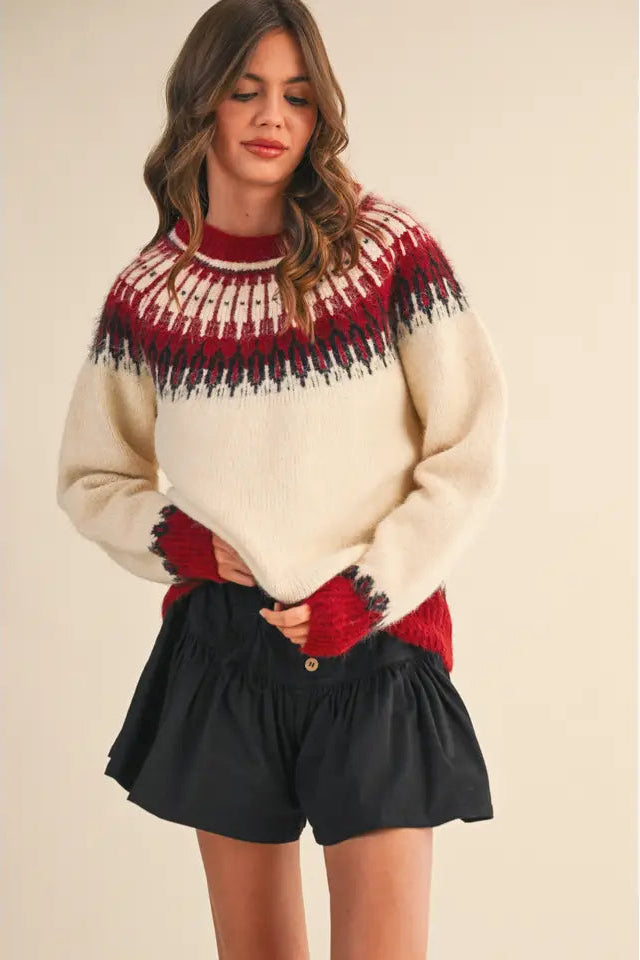 Woman wearing a cream sweater with red and black pattern and black shorts on a beige background