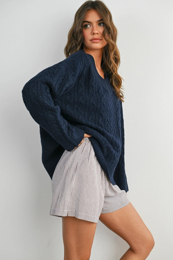 Girl Standing against a plain background wearing a V neck Navy Blue cable knit sweater with long sleeve