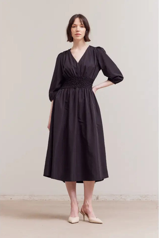 Woman wearing a black dress with a belt against a plain background