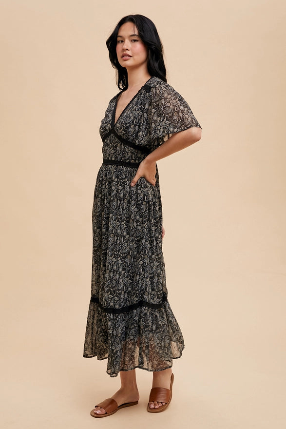 Woman wearing a black midi dress with flutter sleeves on a plain background