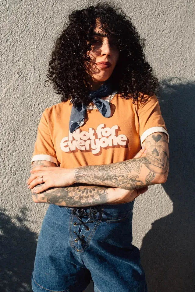 Person wearing an orange t-shirt with text, standing against a textured wall.