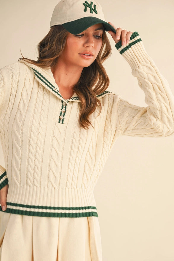 Woman wearing a cream cable knit sweater and green and white cap on a beige background