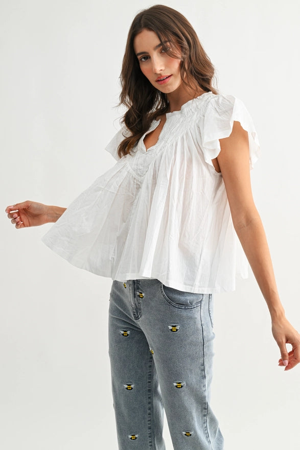 Woman wearing a white blouse with ruffled sleeves and light blue jeans on a plain background