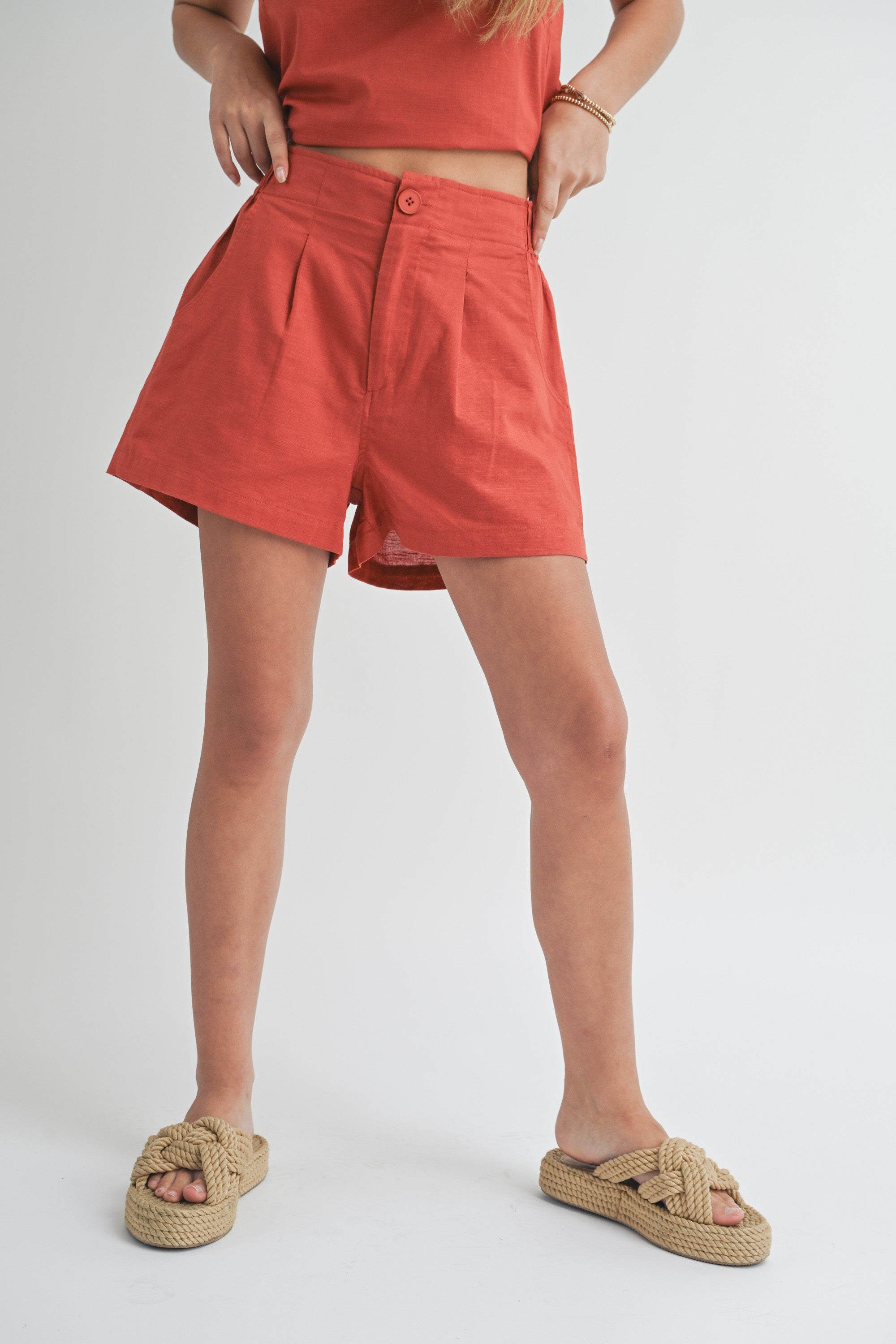 A person standing wearing red shorts with an elastic waistband and white sandals.