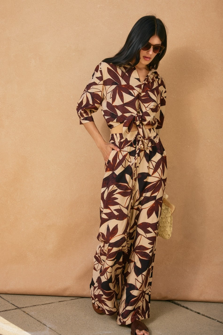 Woman wearing a patterned jumpsuit against a beige wall