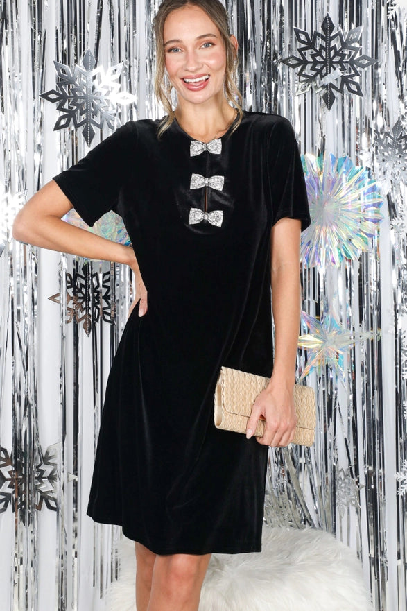 Woman wearing a black dress with silver buttons against a decorative silver and black background.