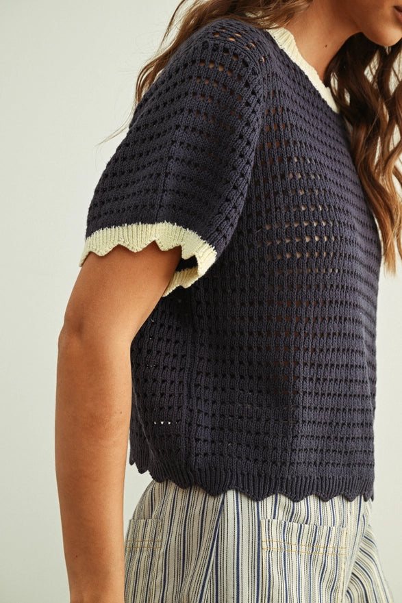 Person wearing a navy blue crochet top with white trim on a plain background