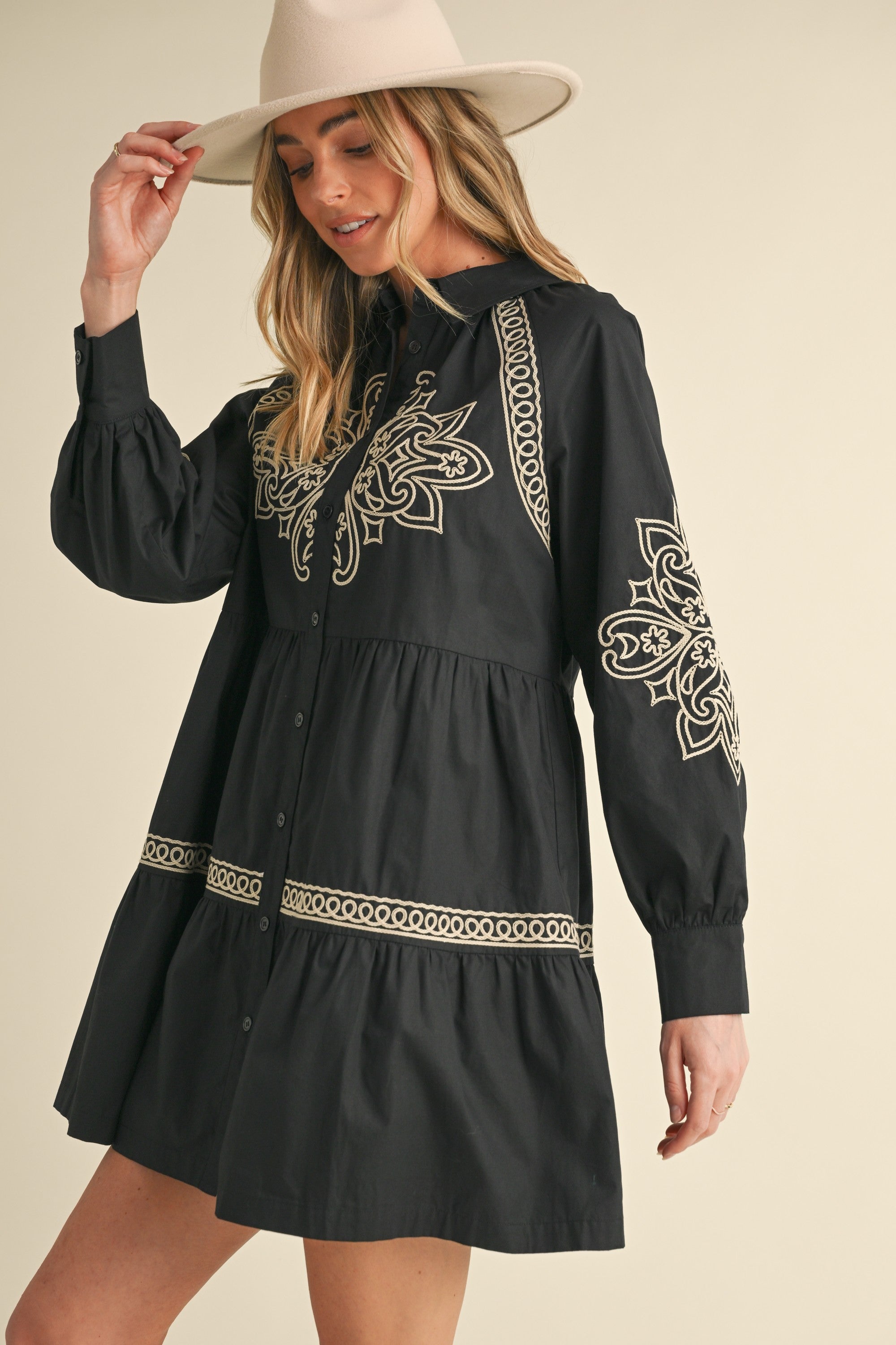 Woman wearing a black dress with intricate white embroidery on a beige background