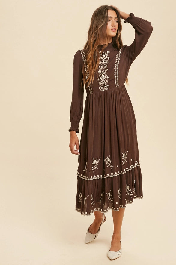 Woman wearing a brown dress with floral embroidery on a beige background