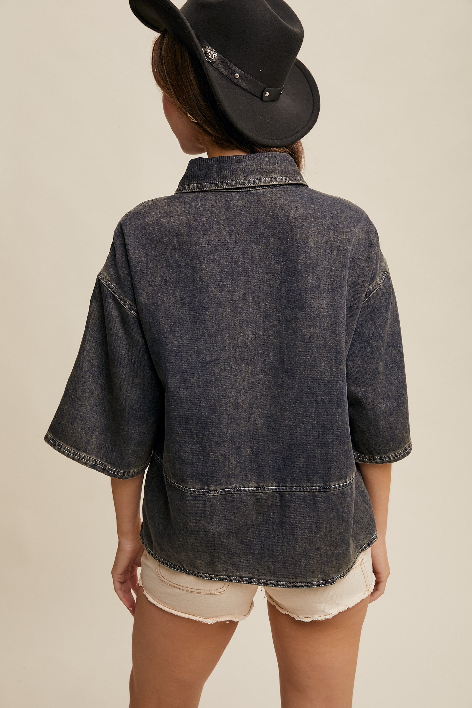 Person wearing a dark denim jacket and black cowboy hat on a beige background