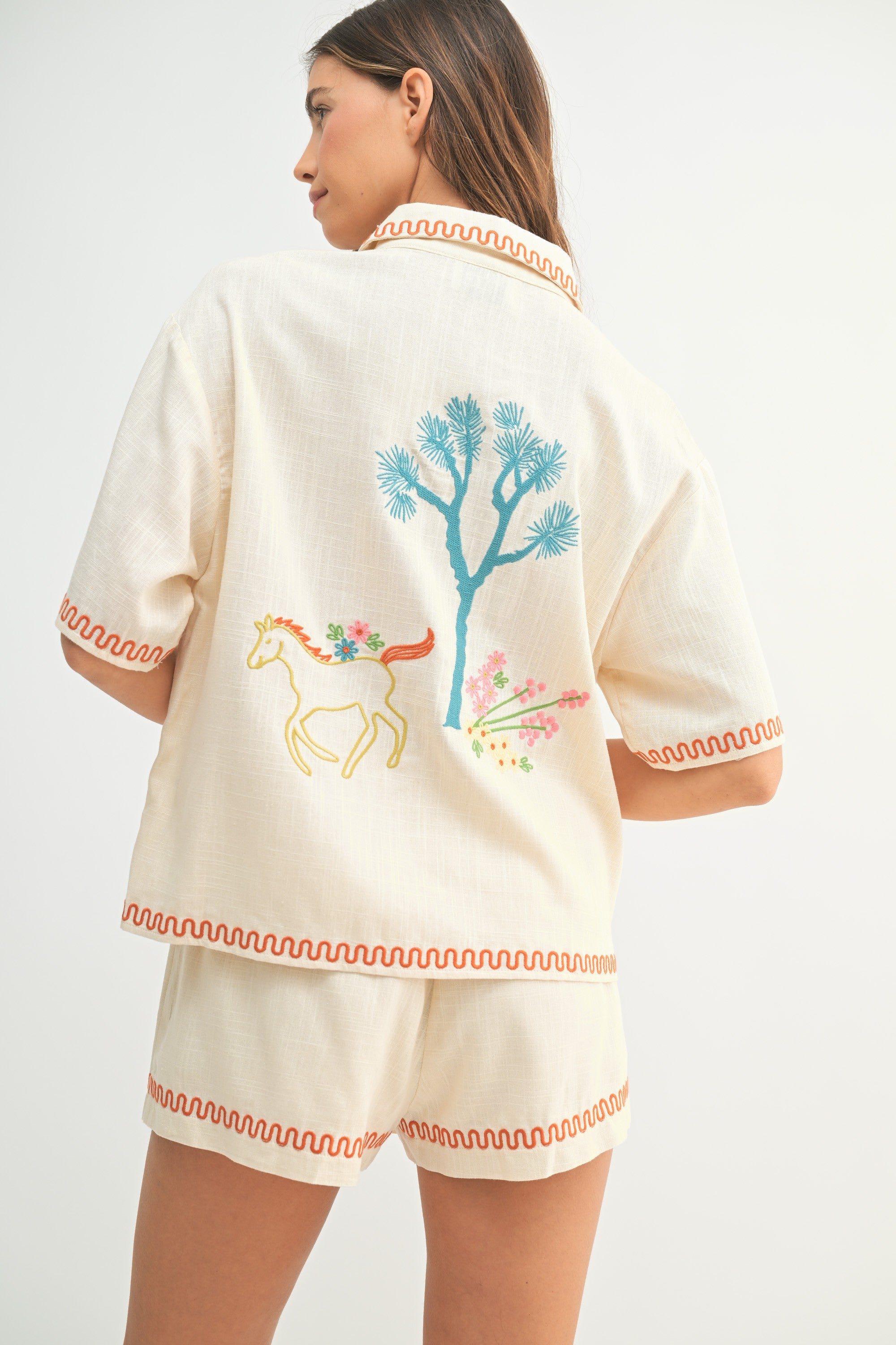 Woman wearing a cream-colored outfit with embroidered designs on a white background