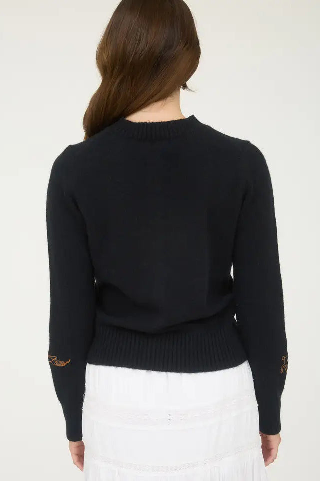 Person wearing a black sweater with gold accents on a white background