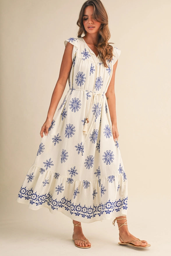 Woman wearing a white dress with blue floral patterns on a plain background