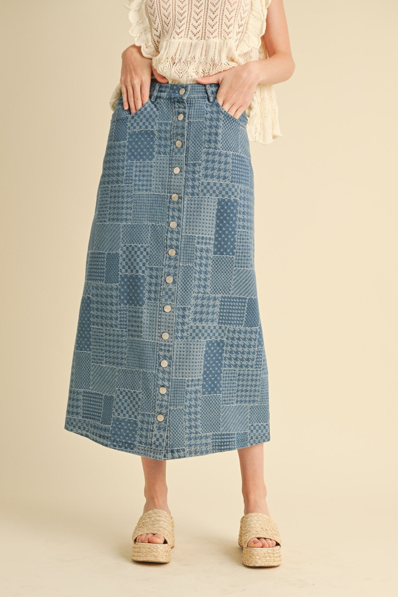Person wearing a blue patchwork skirt with button details on a beige background