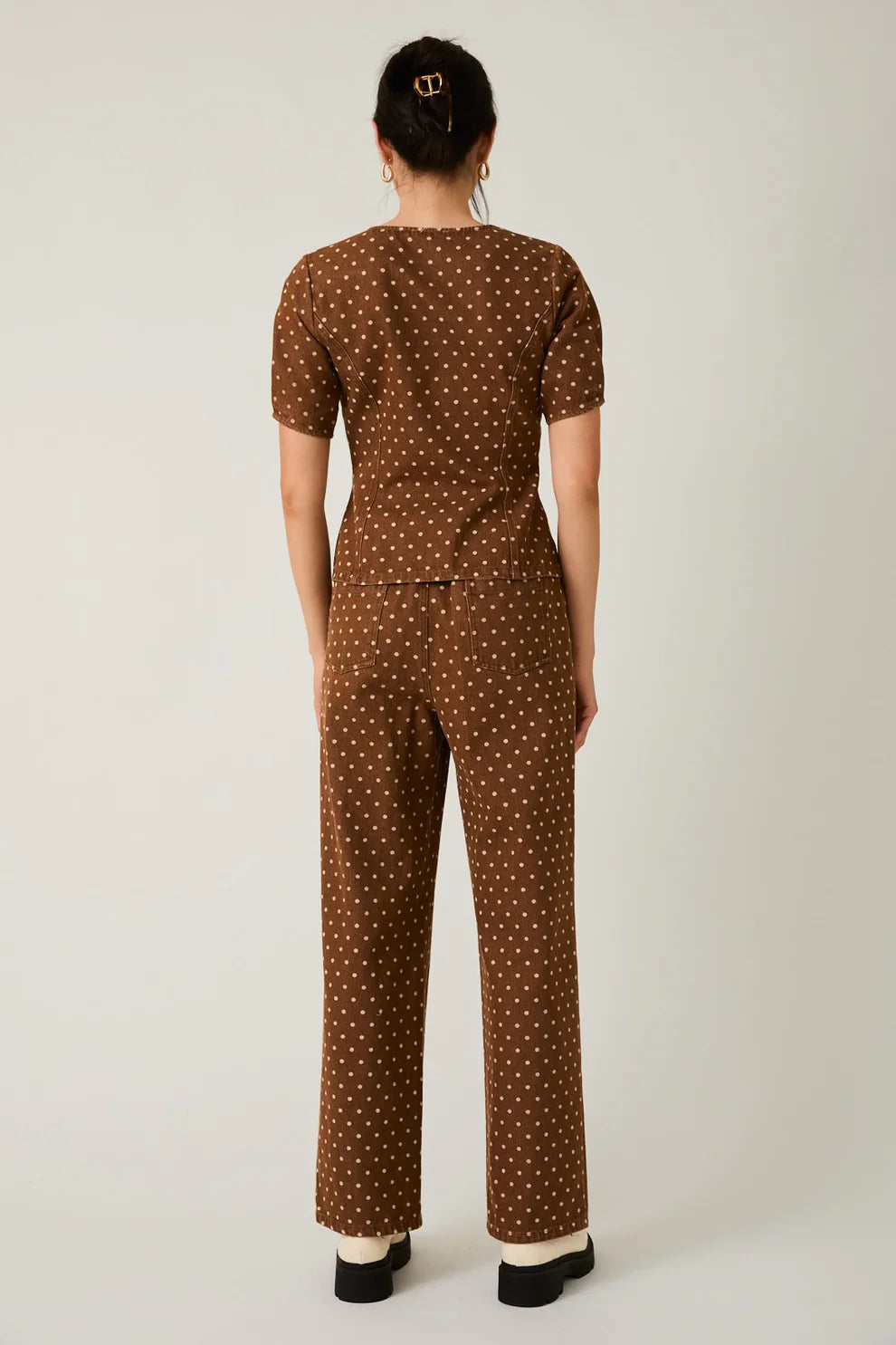 Person wearing a brown polka dot jumpsuit on a light background