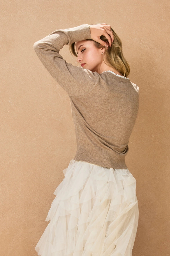 Woman wearing a brown sweater and white skirt against a beige background