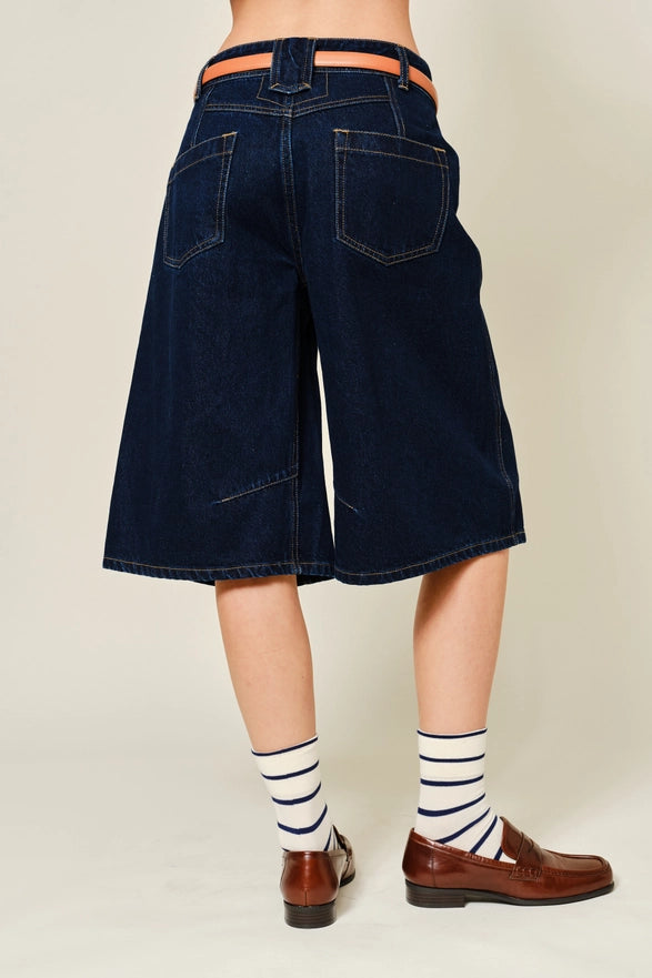 Person wearing dark denim shorts with a plain background