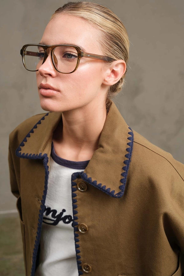 Person wearing a brown jacket with blue trim and glasses against a neutral background