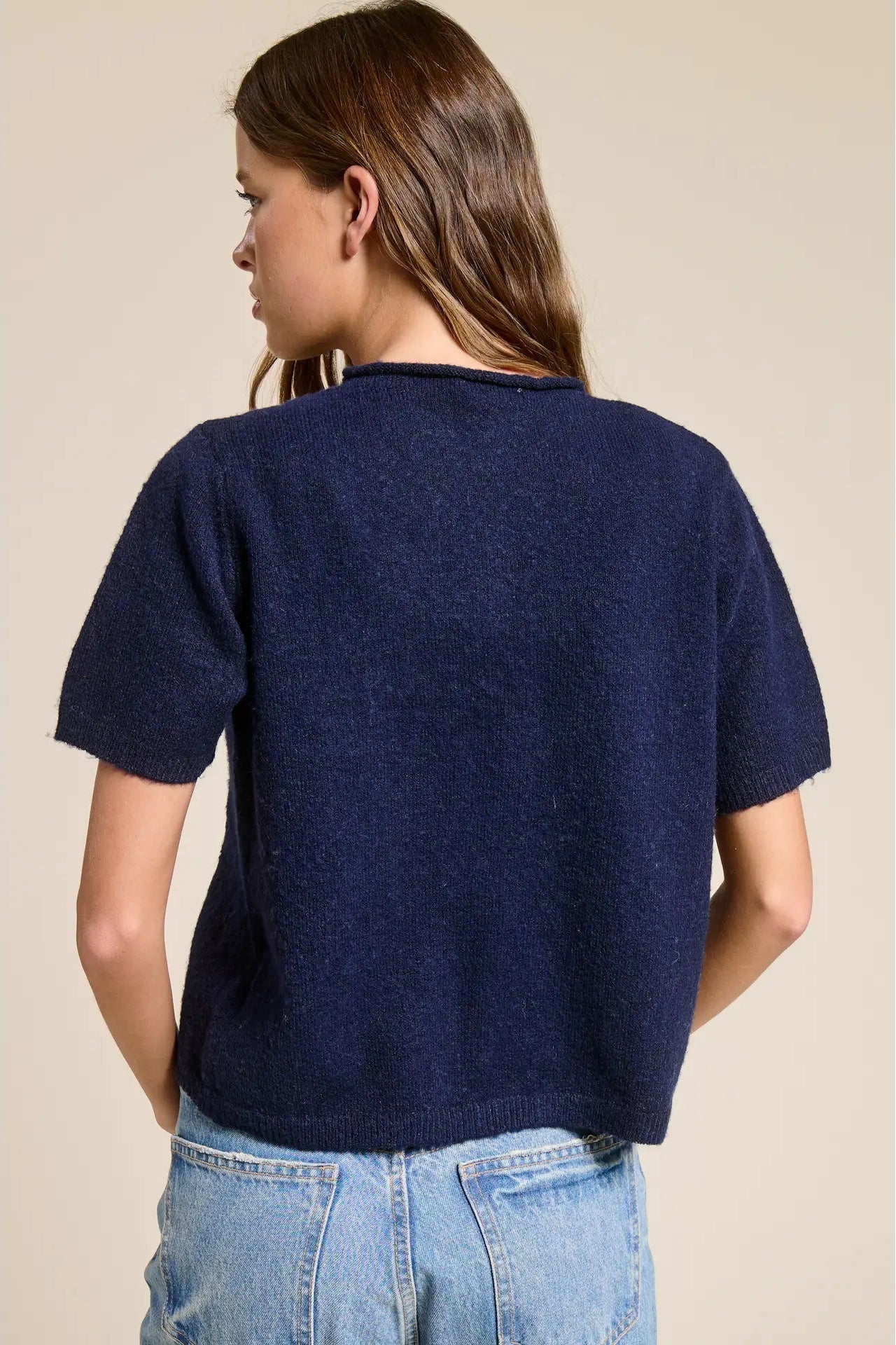 Person wearing a navy blue t-shirt and light blue jeans on a beige background