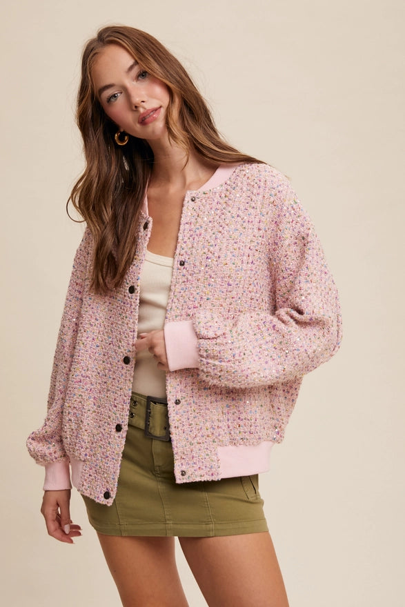 Woman wearing a pink textured cardigan over a white top and green shorts on a beige background