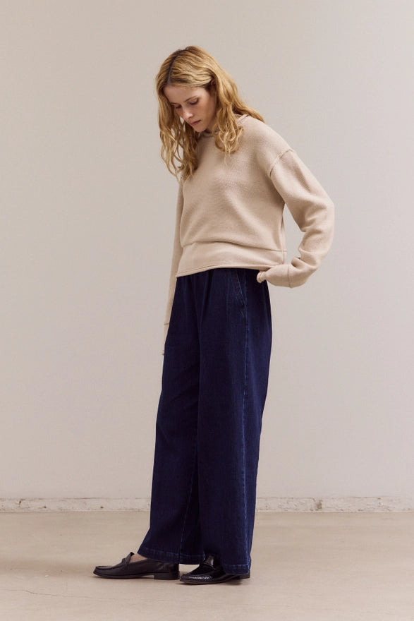 Woman wearing a beige sweater and navy pants against a plain background