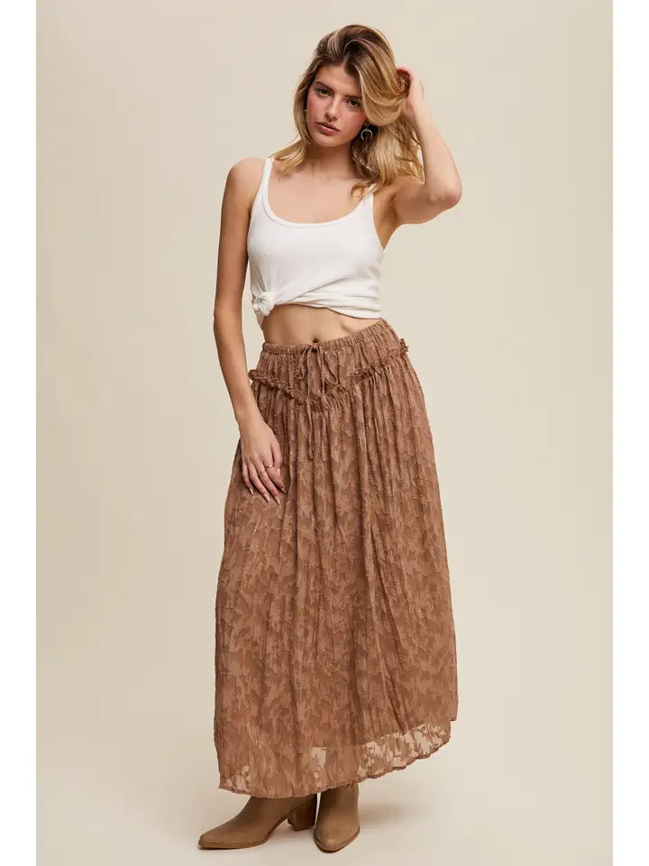 Woman wearing a white tank top and brown long skirt against a beige background