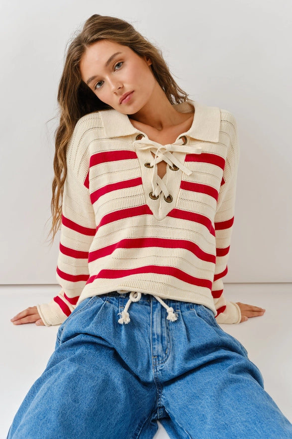 Woman wearing a red and white striped sweater with a lace-up front, sitting against a white background.