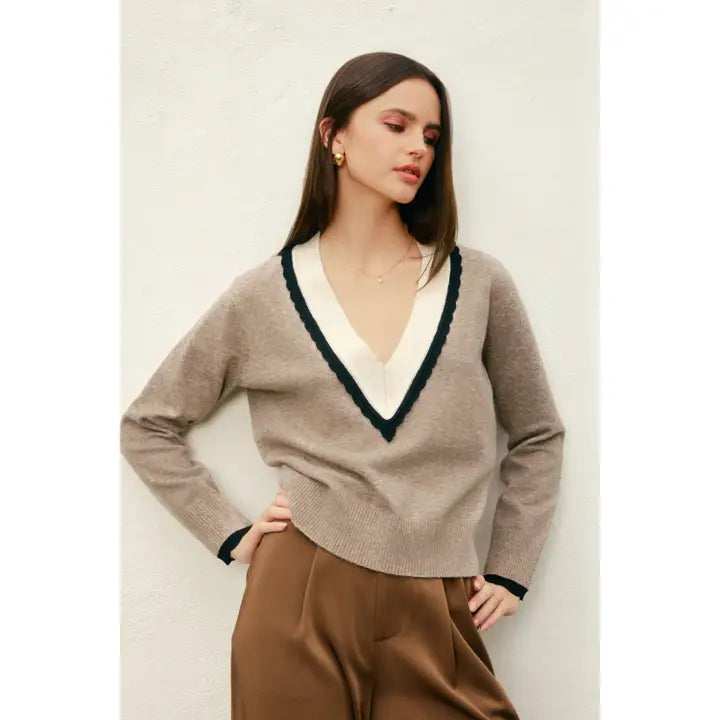 Woman wearing a beige sweater with white neckline and brown pants against a light background