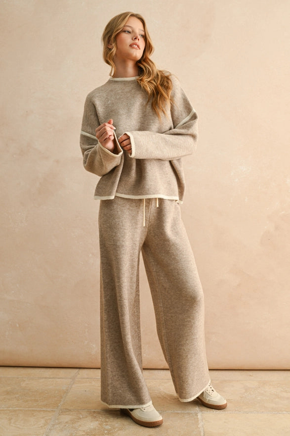 Woman wearing a beige sweater and pants set against a plain background
