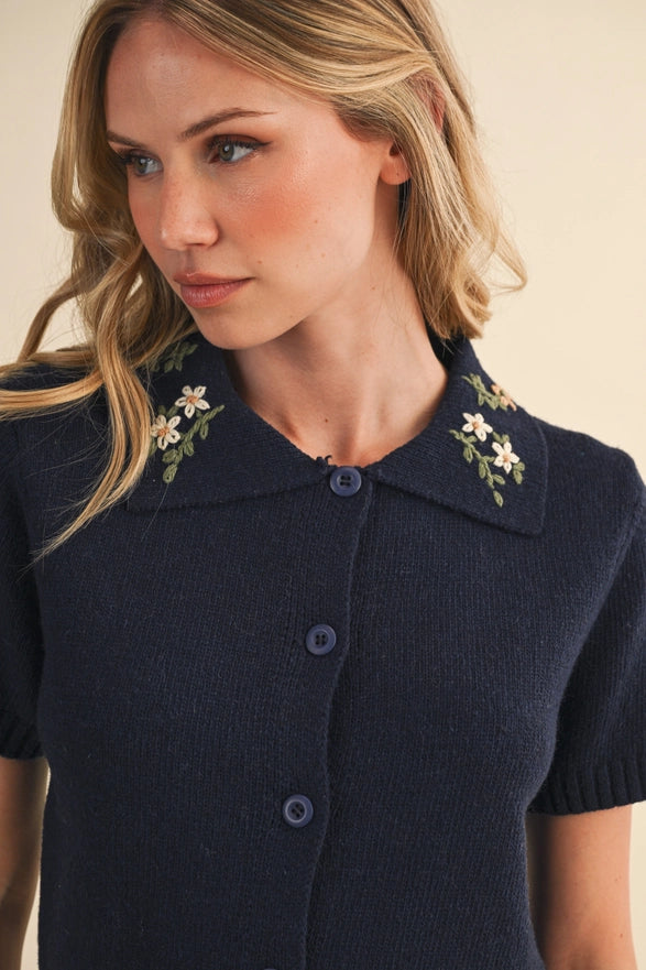 Woman wearing a navy blue dress with floral embellishments on the collar against a beige background