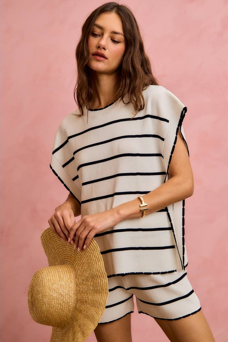 Woman wearing a black and white striped dress holding a straw hat against a pink background