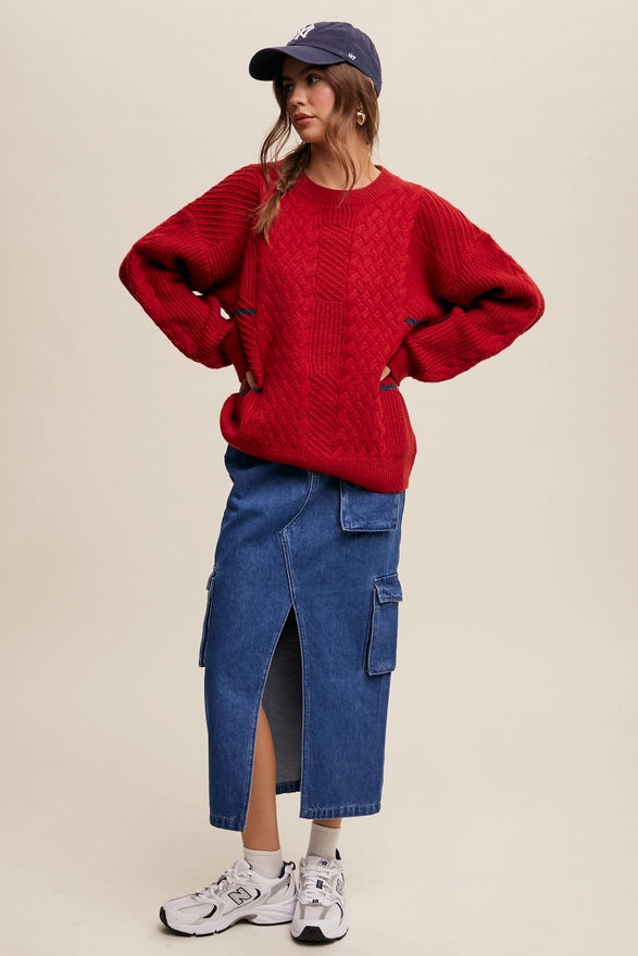 Woman standing against a plain background wearing a Red pull over sweater