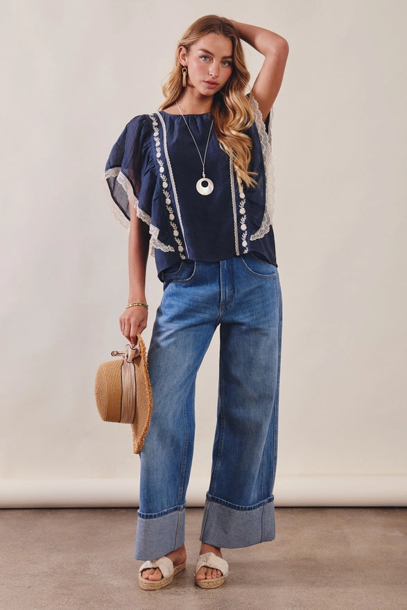 Woman wearing a navy top with white trim and blue jeans, holding a beige handbag.