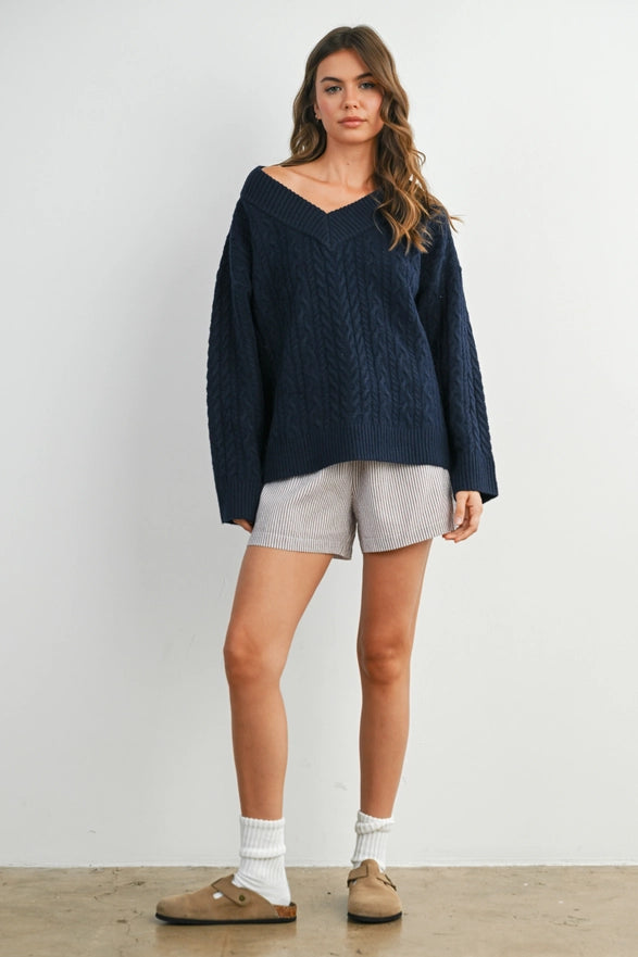 Girl Standing against a plain background wearing a V neck Navy Blue cable knit sweater with long sleeve