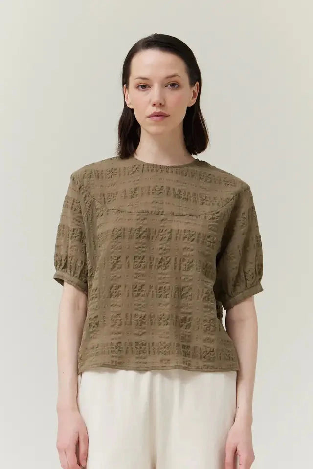 Woman wearing a textured green top against a plain background