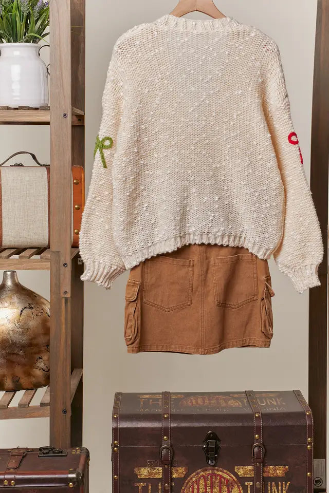 Beige knitted sweater with text and brown skirt hanging on a wooden rack with decorative items.