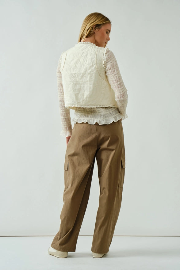 Woman wearing a cream quilted jacket and beige cargo pants on a white background