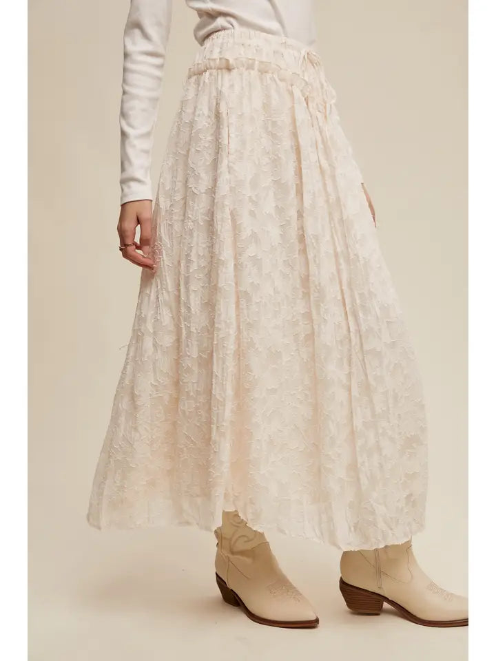 Person wearing a light-colored lace skirt and white boots on a plain background