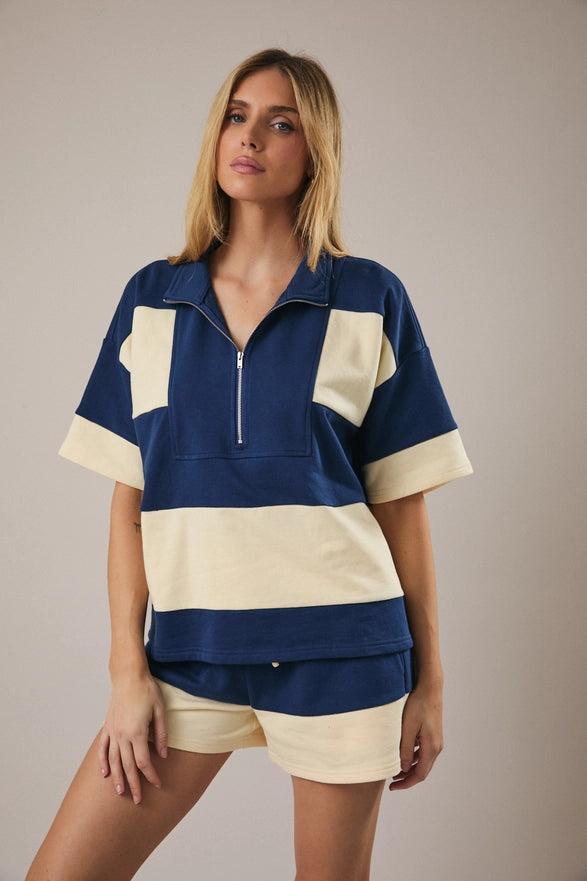 Model is wearing a matching cream and navy striped set with shorts and a half zip polo like top.