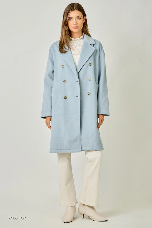 Woman wearing a light blue coat with gold buttons on a white background