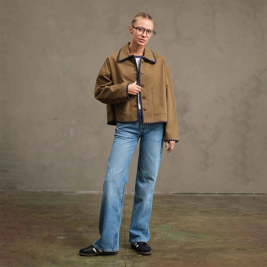 Person wearing a brown jacket and blue jeans against a plain background