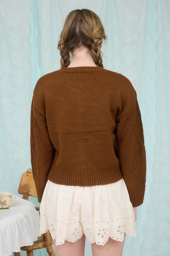 Person wearing a brown sweater and white lace skirt against a light blue curtain background