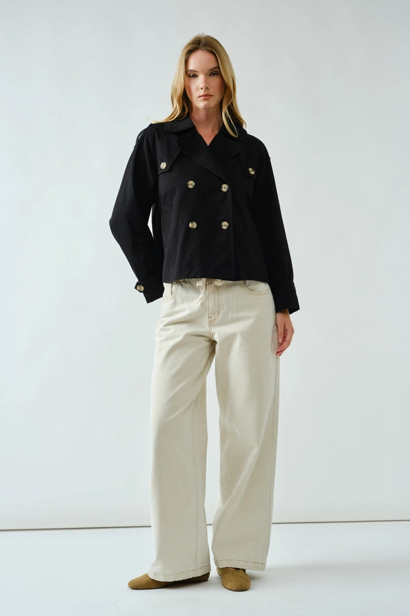 Woman wearing a black jacket with gold buttons and beige pants on a white background