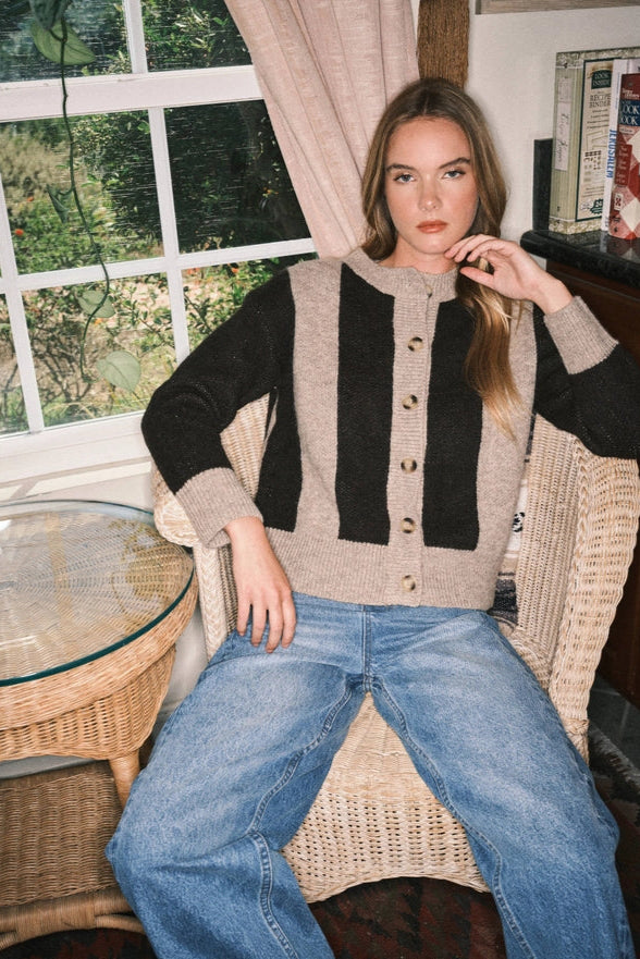 Woman wearing a black and beige cardigan and blue jeans sitting on a wicker chair.