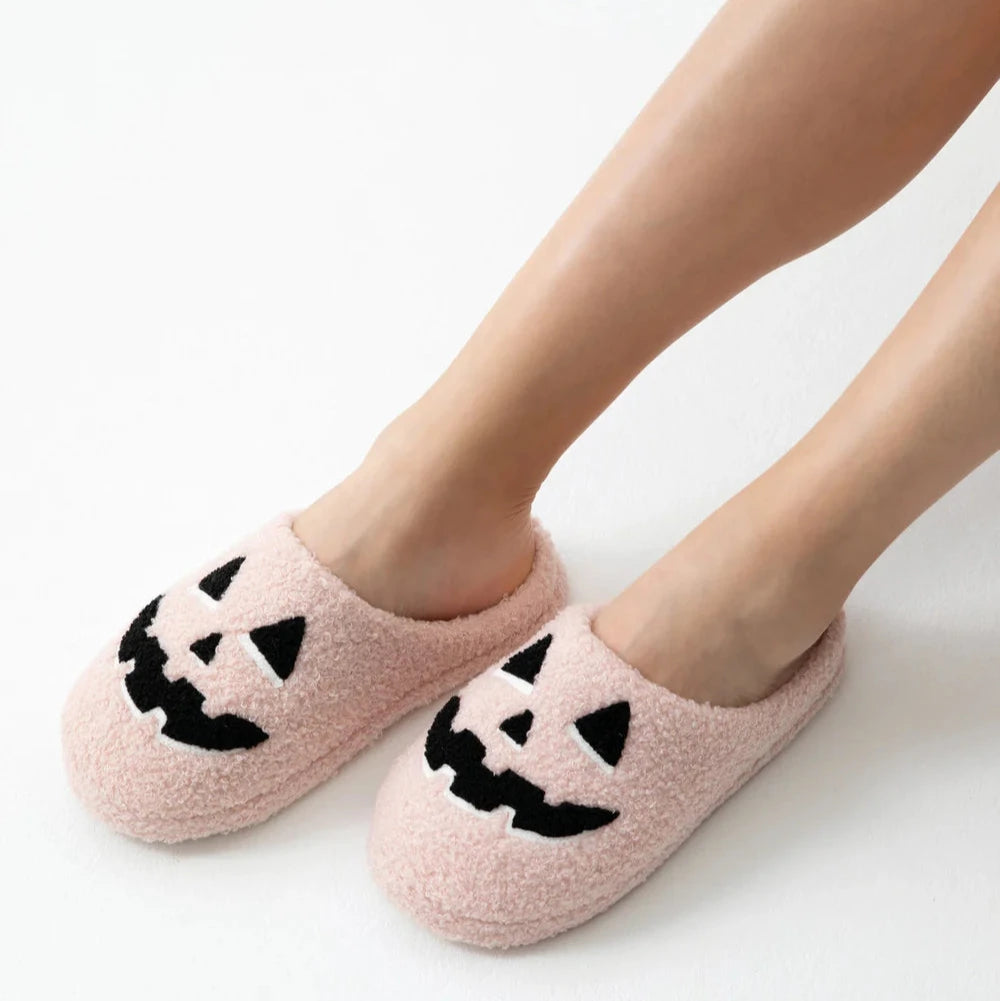 Pink slippers with black jack-o'-lantern faces worn by a person on a white background