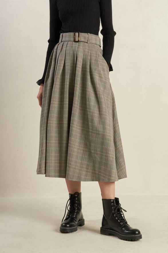 Person wearing a plaid skirt and black boots on a beige background
