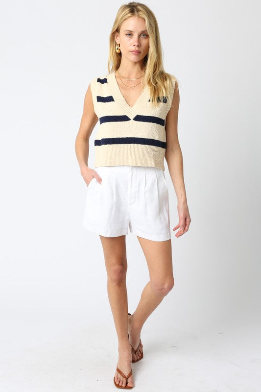 Woman wearing a striped sleeveless top and white shorts on a plain background