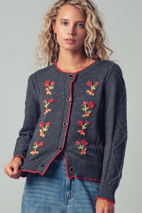 Woman wearing a dark gray cardigan with floral embroidery on a plain background