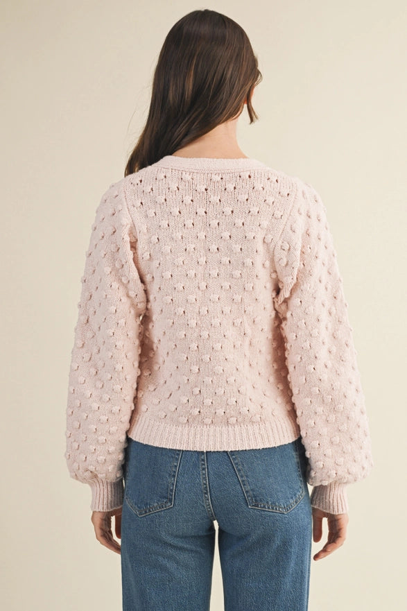 Person wearing a light pink textured sweater and blue jeans on a beige background